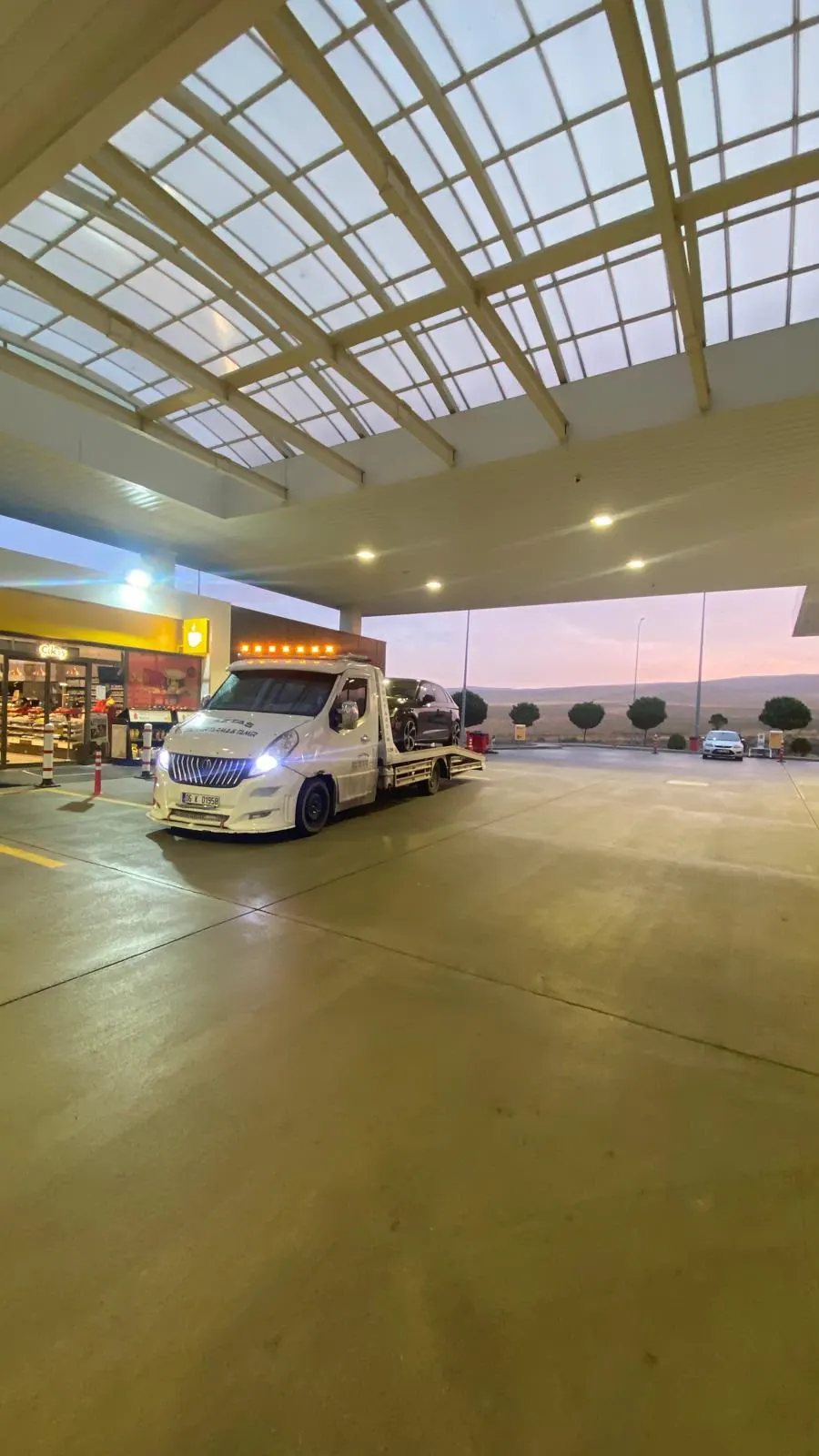 Gün doğarken otoyol dinlenme tesisinin sundurması altında bekleyen oto çekici.