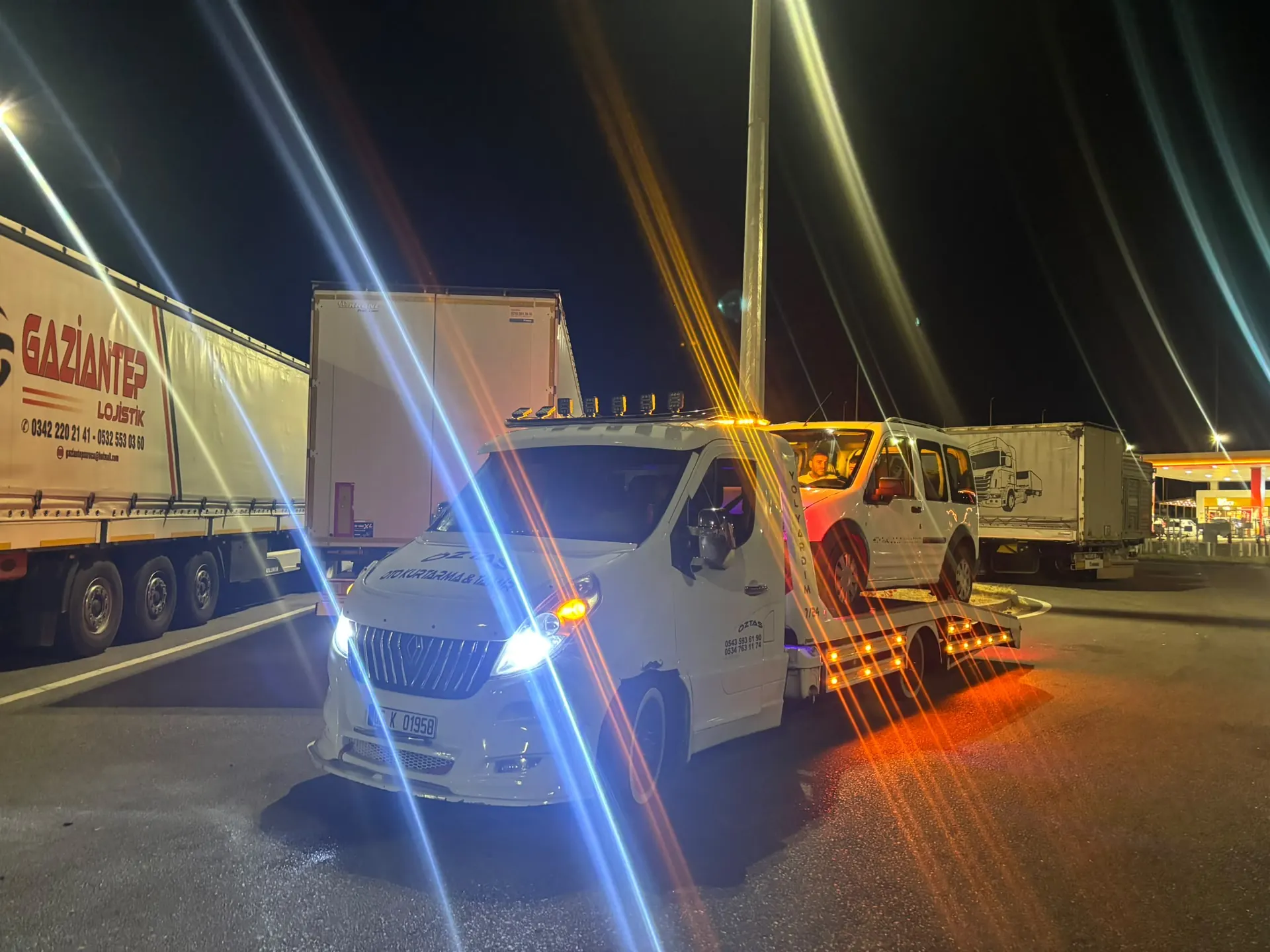 Gece tır parkında tırların arasında duran oto çekici, platformunda hafif ticari araç.